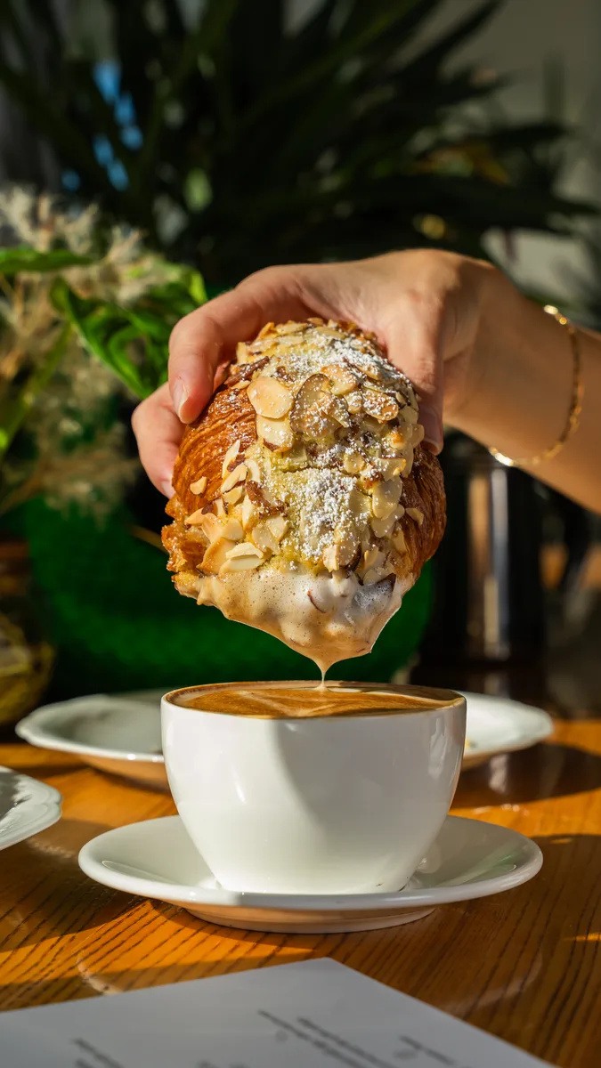 Almond croissant being dipped into a latte at Madame Olivia