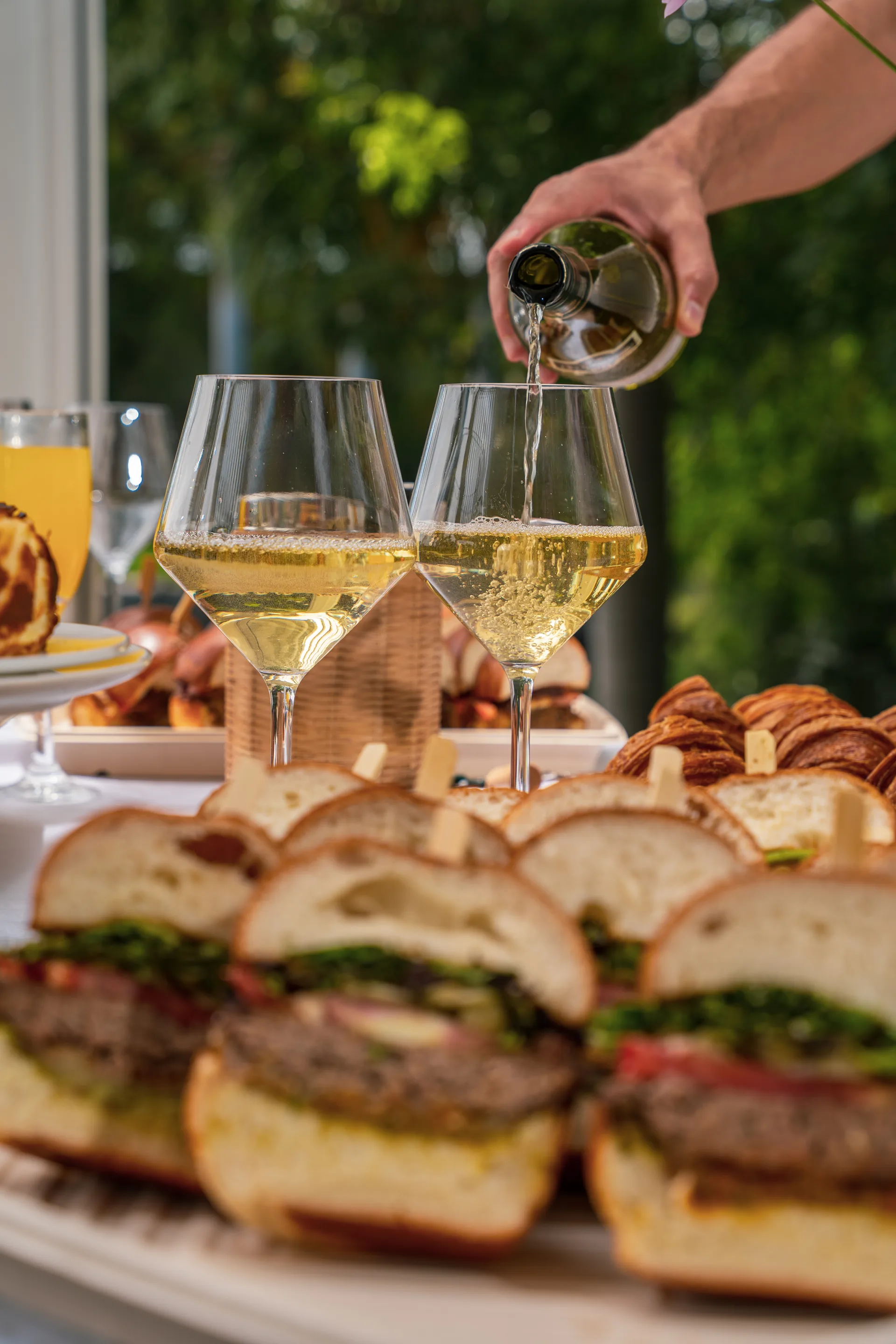 Wine being poured over catering spread with sandwiches and croissants