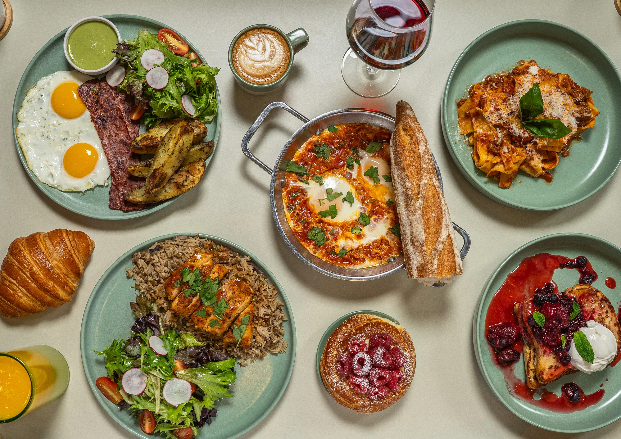 Overhead spread of dishes at Madame Olivia: chicken, shakshuka, bolognese, berry French toast, and an egg plate