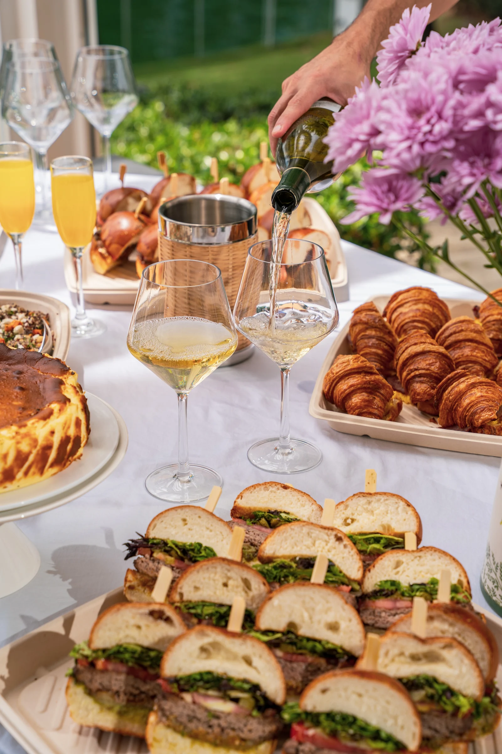 Madame Olivia catering spread with wine pour, croissants, sandwiches, and Basque cheesecake